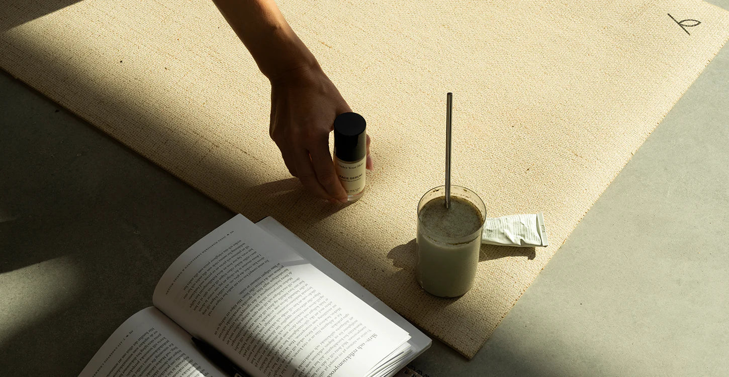 book, drink and woman grabbing face serum from the yoga mat.
