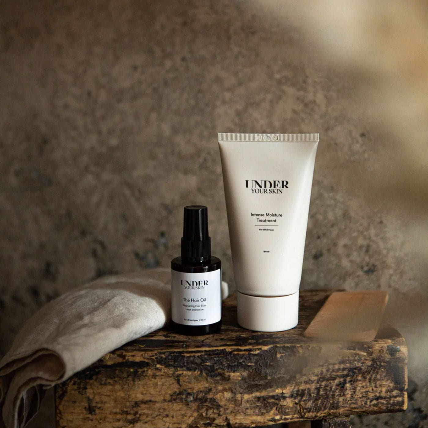 Hårmask och hårolja på en gammal träbänk tillsammans med en träkam och en linnehandduk i ett badrum.