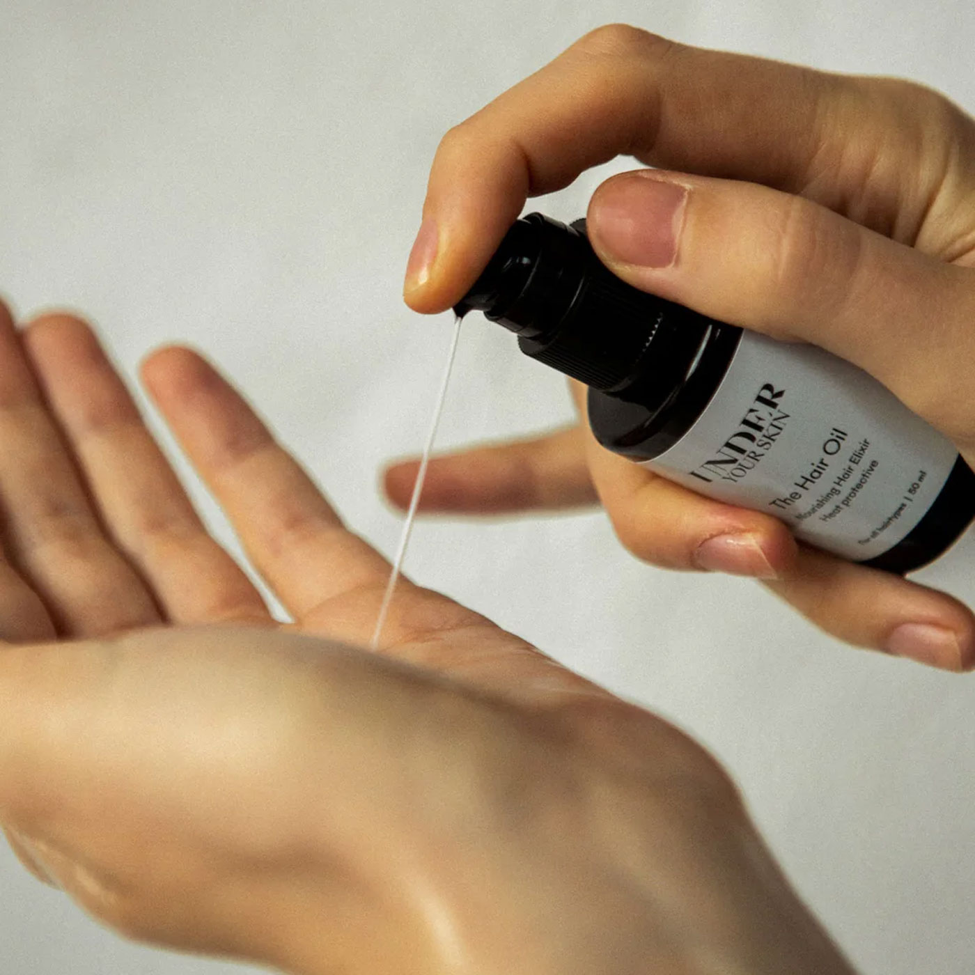 Närbild på händer där hårolja appliceras på ena handen.