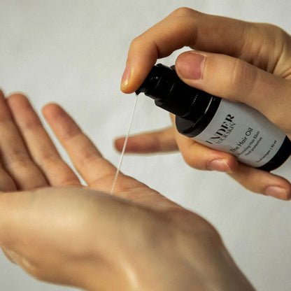 Närbild på händer där hårolja appliceras på ena handen.