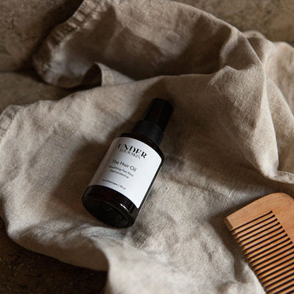 Hårolja liggande på en linnehandduk tillsammans med en träkam bredvid, i badrumsmiljö.