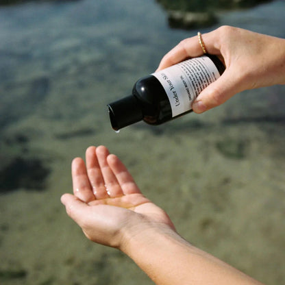 Body oil som hälls på handen med vatten i bakgrunden.