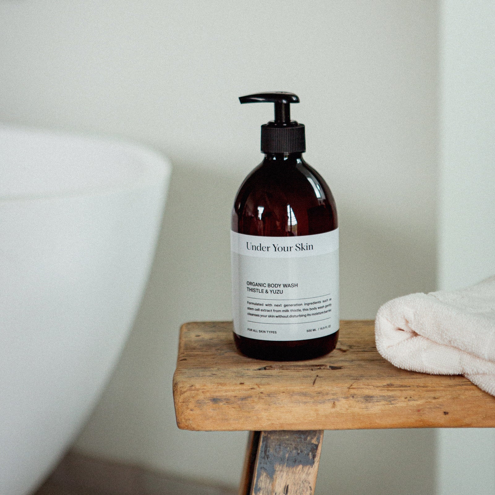 Body wash på en gammal träbänk med en rosa handduk bredvid i badrumsmiljö.