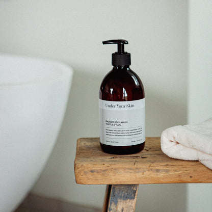 Body wash på en gammal träbänk med en rosa handduk bredvid i badrumsmiljö.