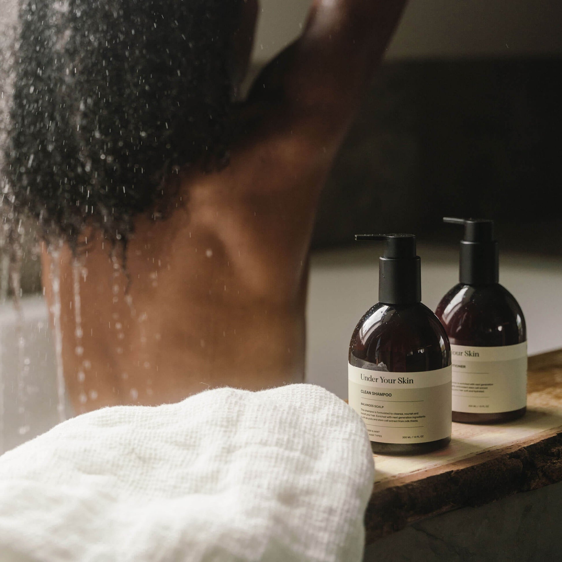 Kvinna i badkar med ryggen mot kameran, hårvårdsprodukter placerade på badkarskanten framför henne.