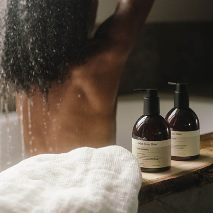 Kvinna i badkar med ryggen mot kameran, hårvårdsprodukter placerade på badkarskanten framför henne.