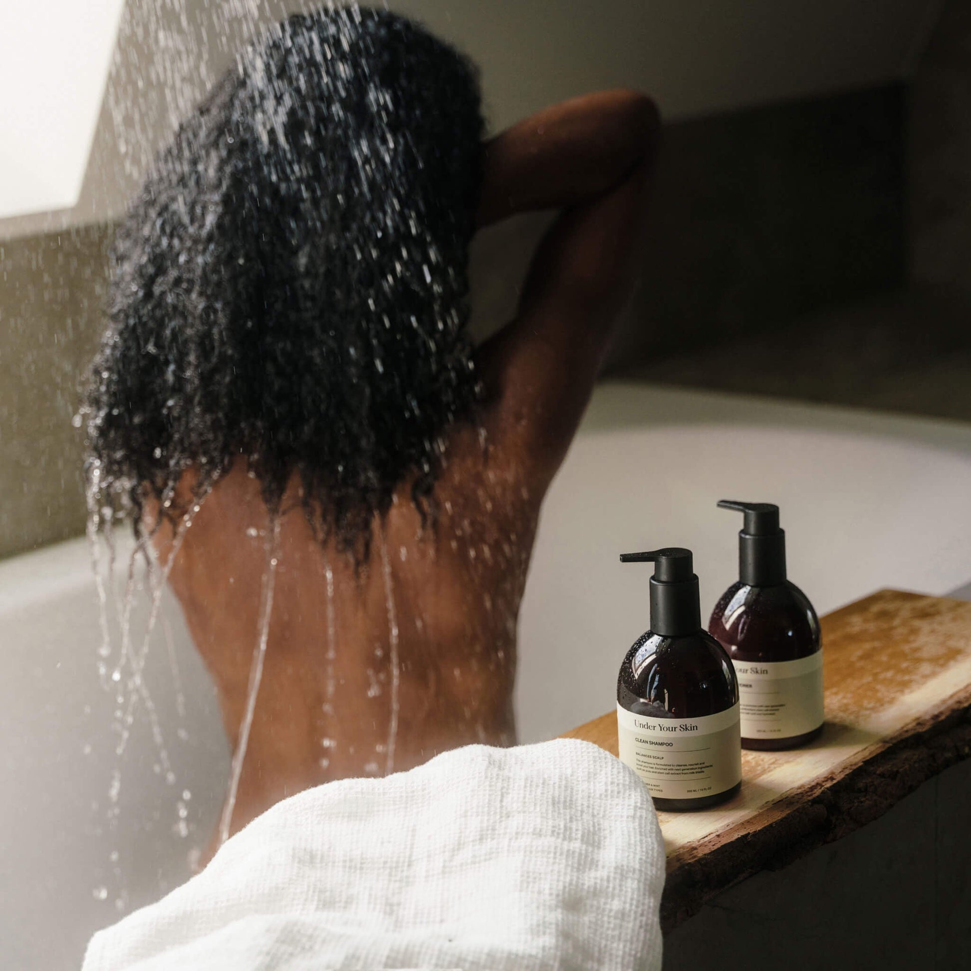 Kvinna i badkar med ryggen mot kameran, hårvårdsprodukter placerade på badkarskanten framför henne.