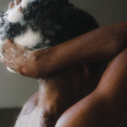 Närbild på person som schamponerar håret, händer masserar in löddrande schampo i blött hår.