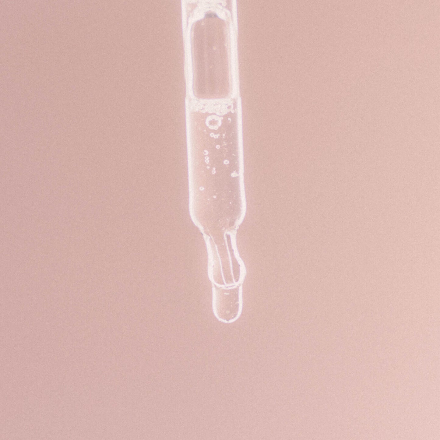 Närbild på en glas­pipett med klar vätska mot en mjuk rosa bakgrund