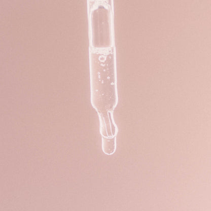 Närbild på en glas­pipett med klar vätska mot en mjuk rosa bakgrund