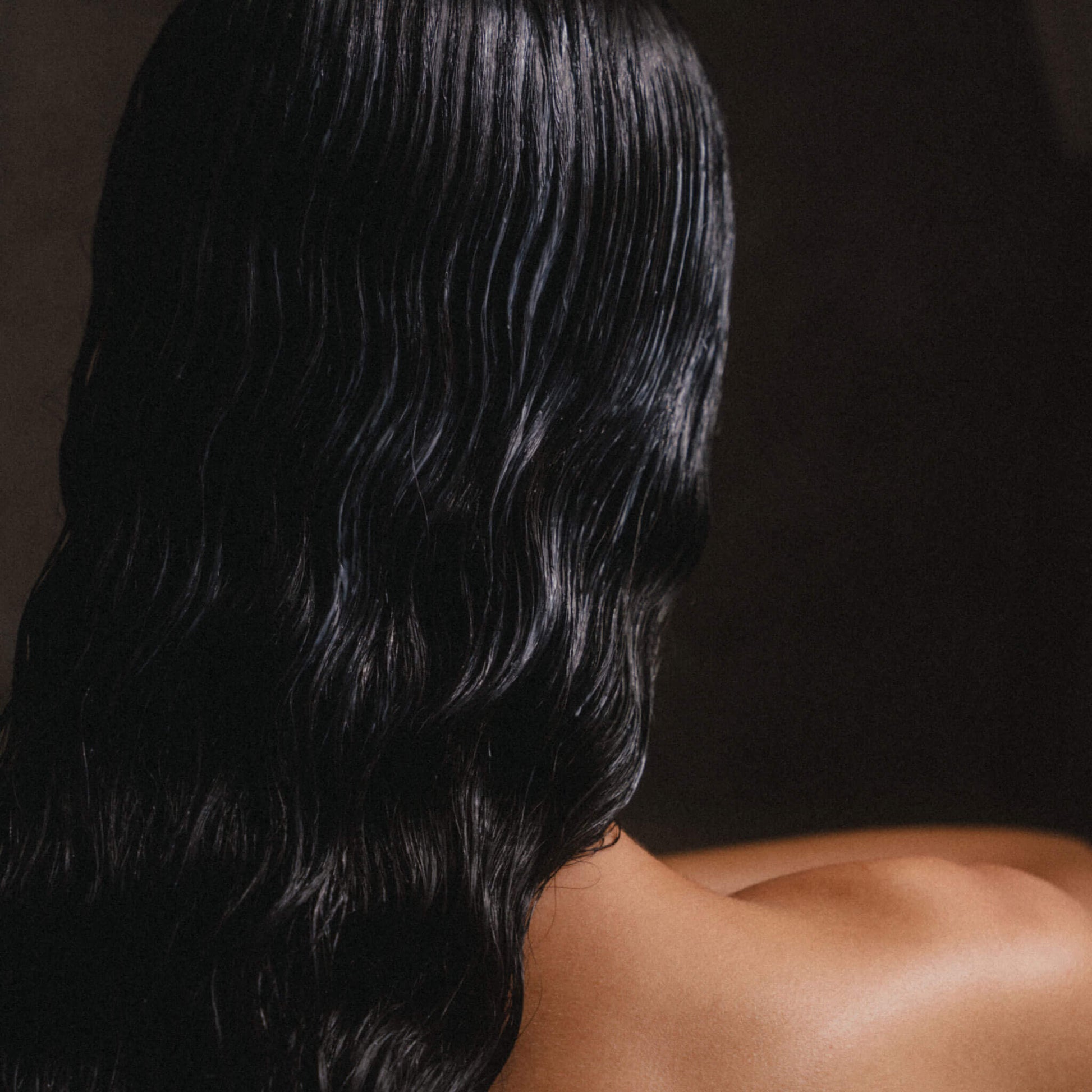 Kvinnas rygg med mörkt, långt hår i badrumsmiljö.