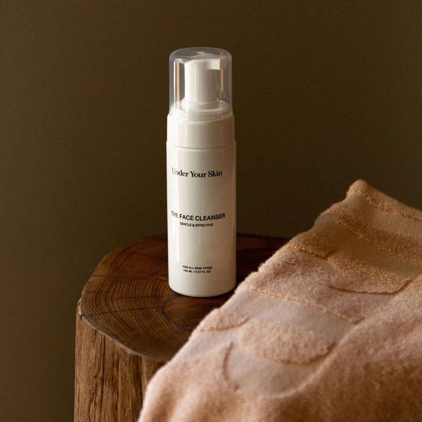 Face cleanser på en träbänk med en rosa handduk framför.