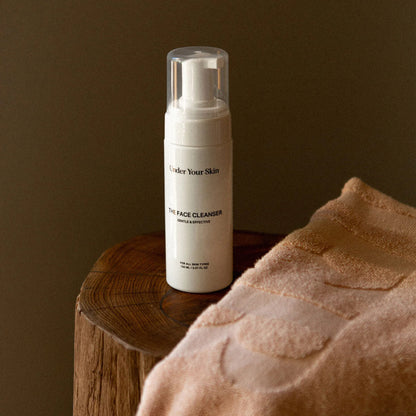 Face cleanser på en träbänk med en rosa handduk framför.