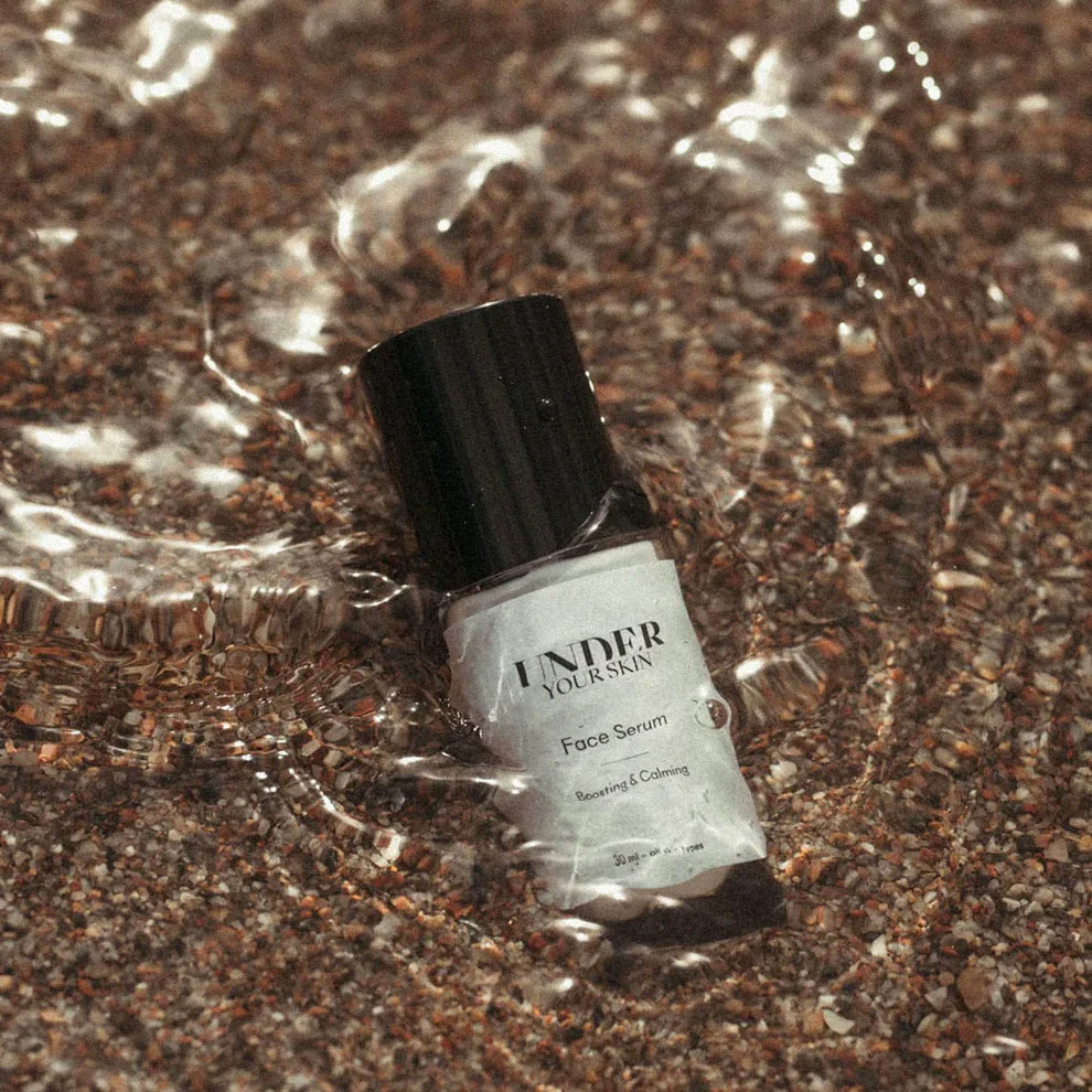 Närbild på Face Serum placerat i strandvatten.