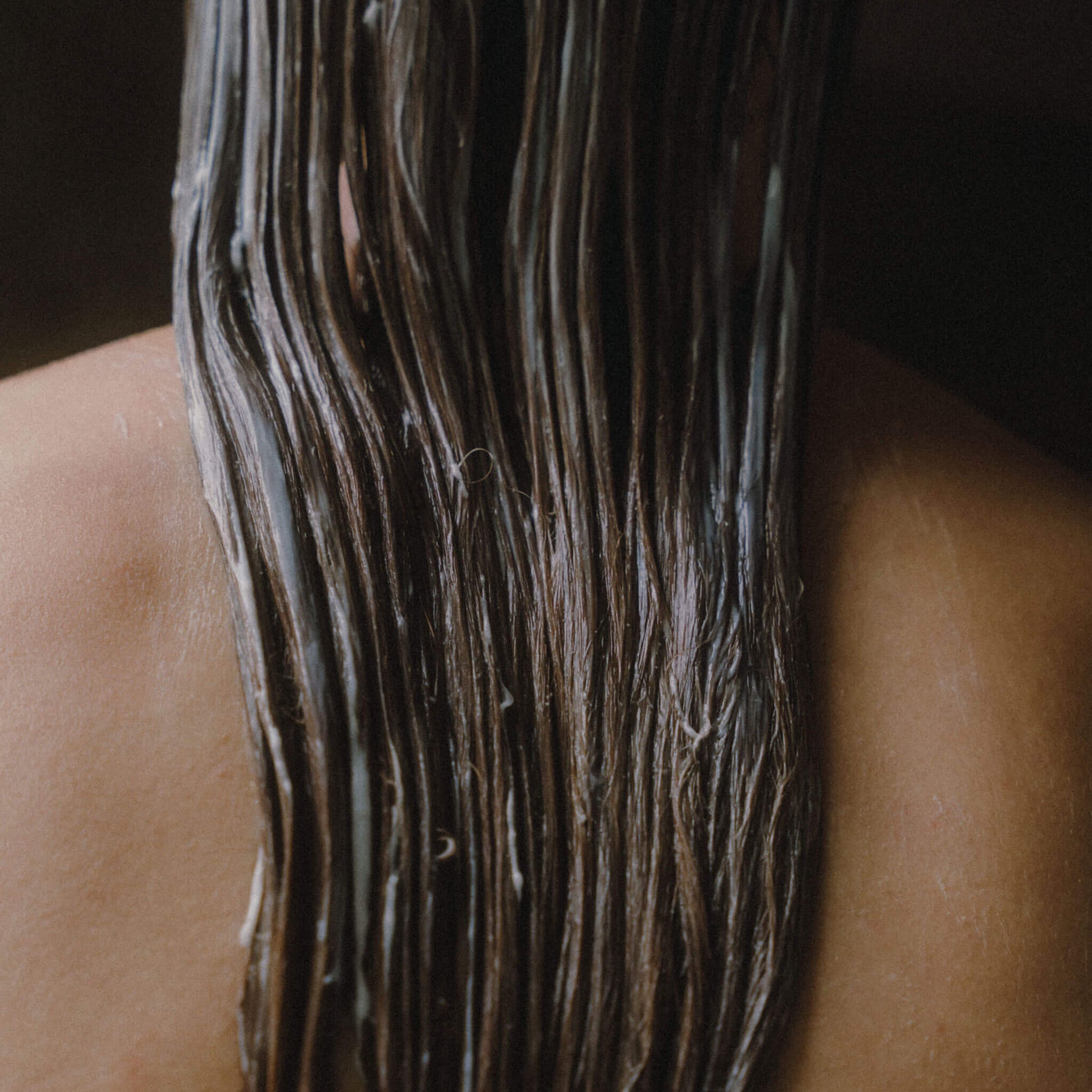 Kvinna som står med ryggen mot kameran med balsam i håret.