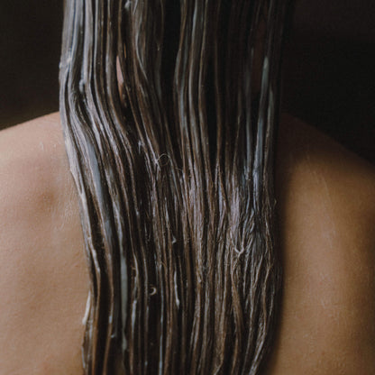 Kvinna som står med ryggen mot kameran med balsam i håret.