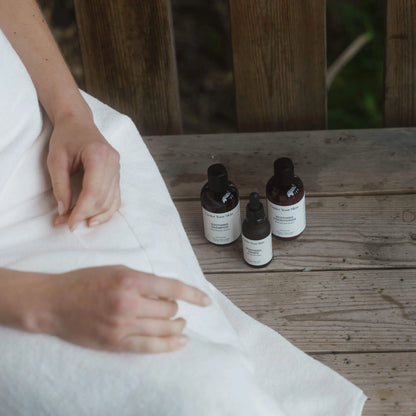 Travel size kit på en bänk bredvid en kvinna som sitter i badrock bredvid produkterna.