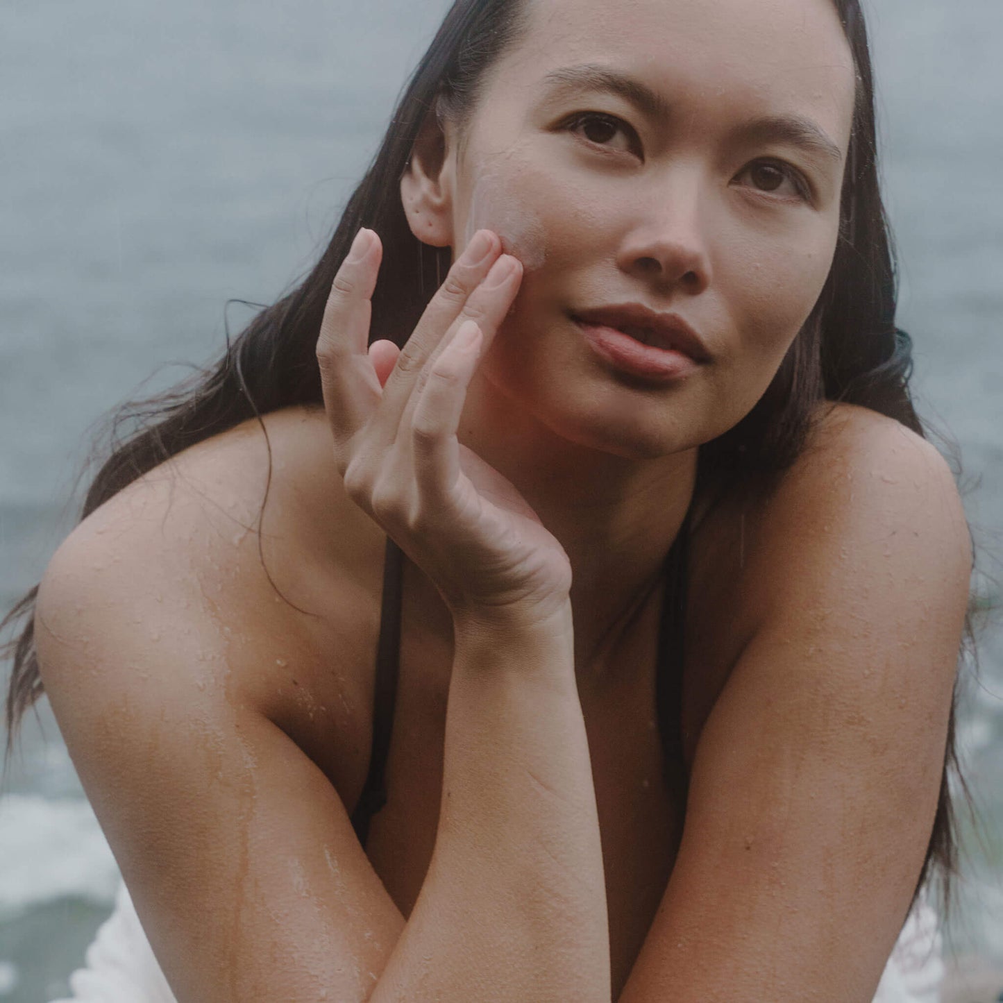 Kvinna som tittar in i kameran medan hon applicerar ansiktsprodukt.