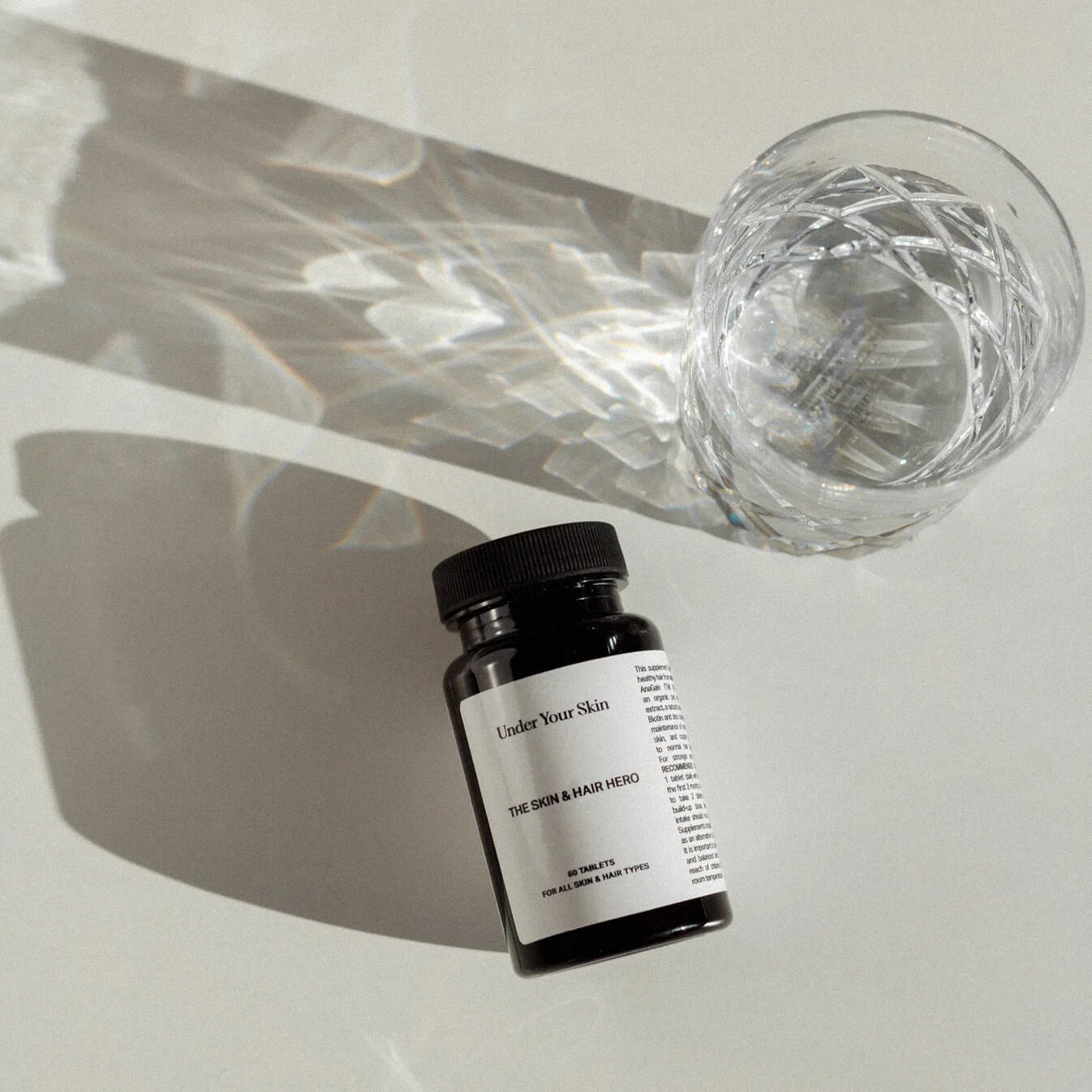 Skin and Hero kosttillskott liggandes på ett bord tillsammans med ett kristallglas på sidan.