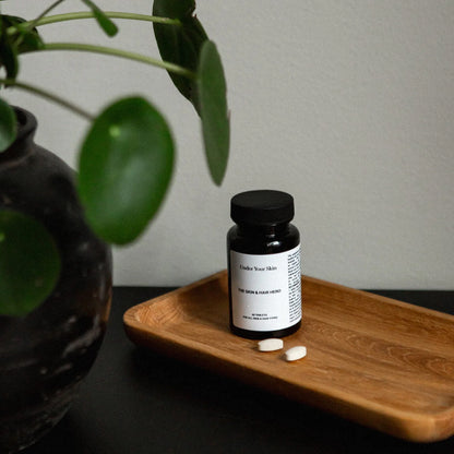 Skin and Hero på en träskål med några tabletter utspridda och en växt suddig i förgrunden på sidan.