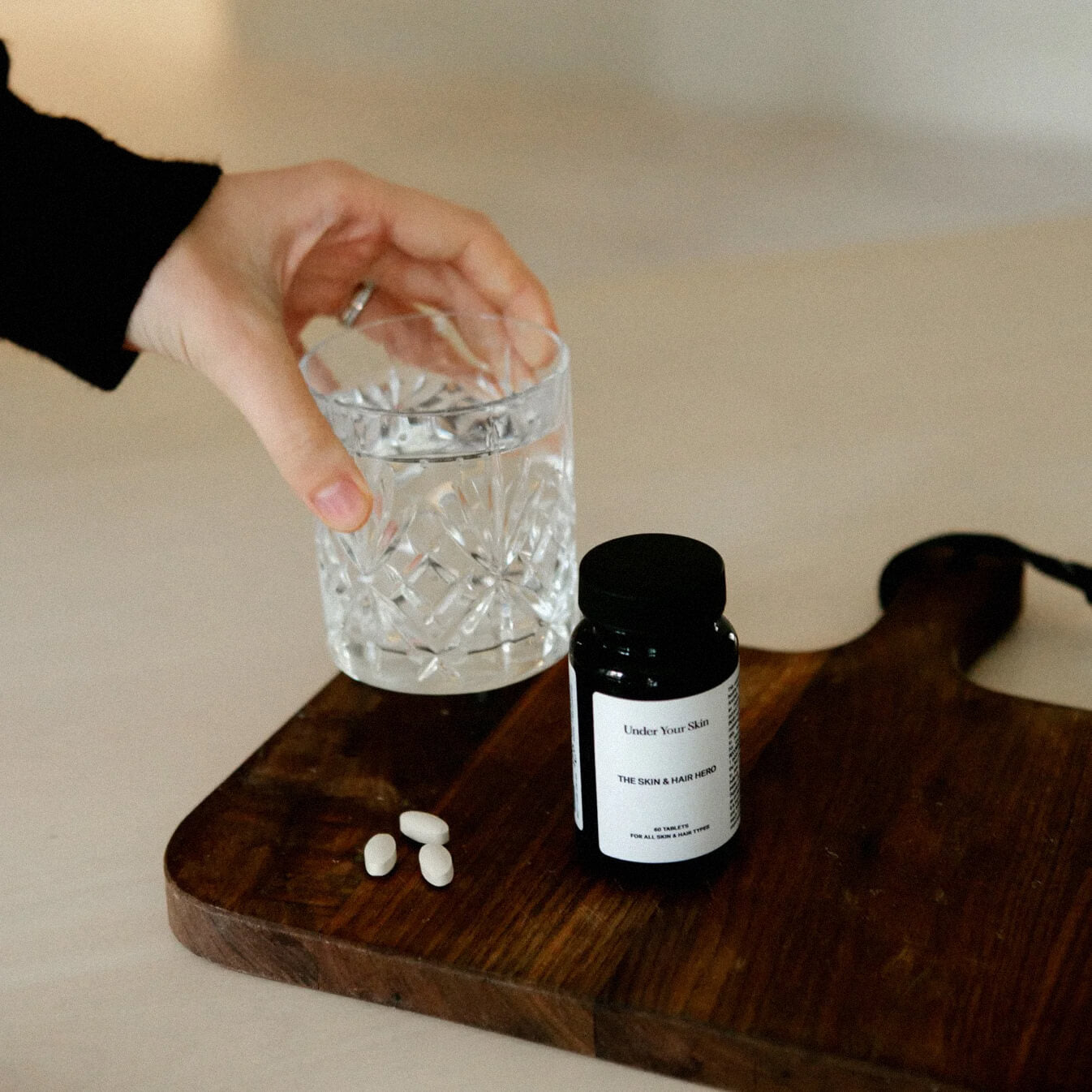 Skin and Hero på en mörk träbit med två tabletter och ett glas som hålls i en hand.