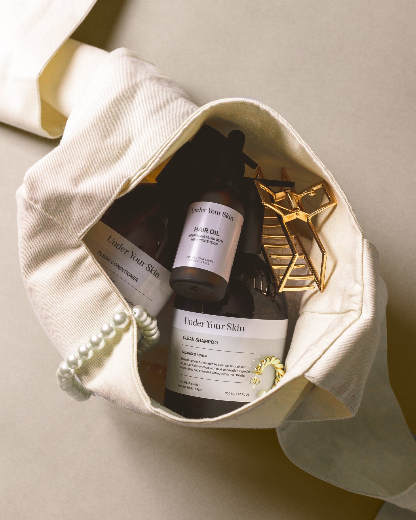 Hårolja, Clean schampo, Clean balsam, hårklämma och pärlhalsband inuti en Bow Bag, fotograferat uppifrån.