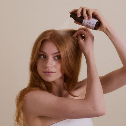 Kvinna sprayar sitt röda hår med torrschampo