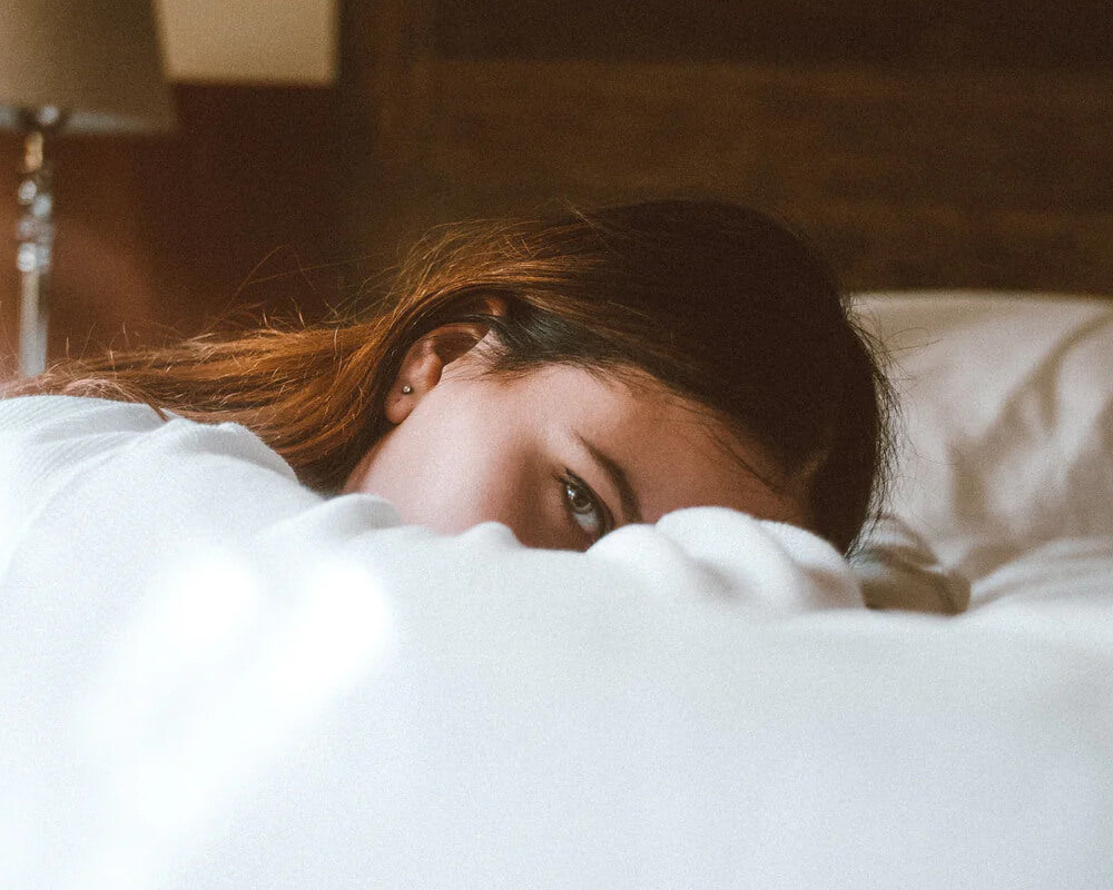 woman laying on the bed, half of her face is covered by blanket.